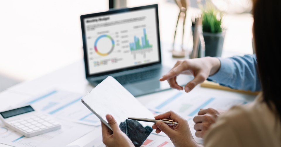 Two professionals collaborating at a busy desk with a laptop displaying skill analytics graphs
